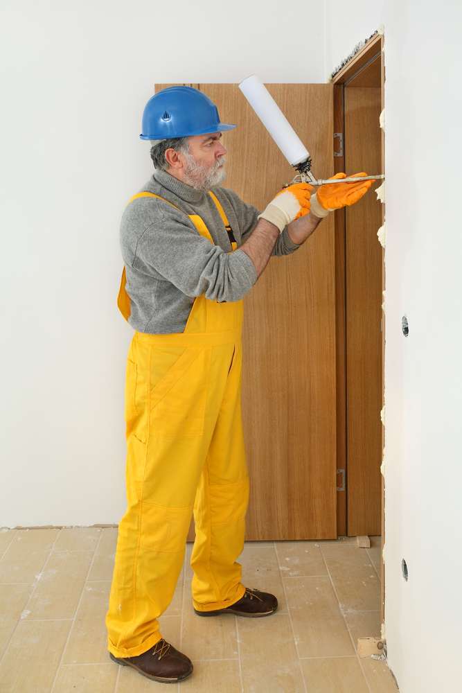 Worker installing wooden door, using polyurethane foam Exterior painting services prep work