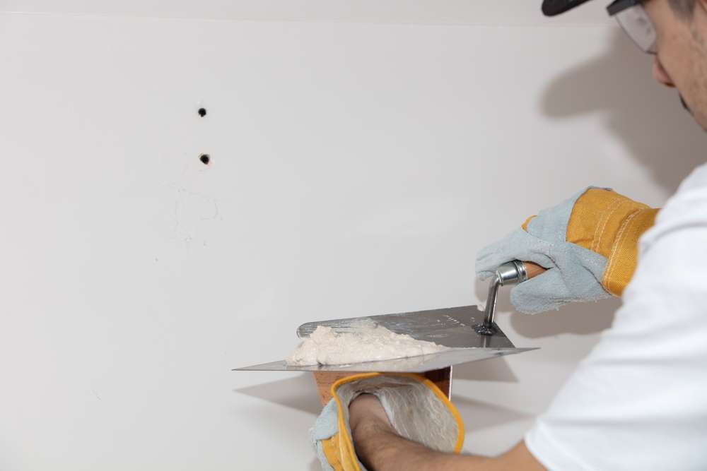 Closeup of a person covering the wall with plaster under the lights Wall prep part of our painting services